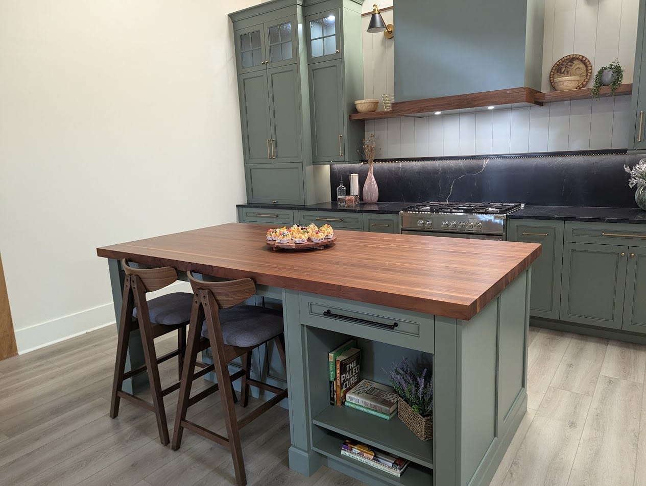 Walnut butcher block island countertop in a sage-green kitchen with a matching floating shelf
